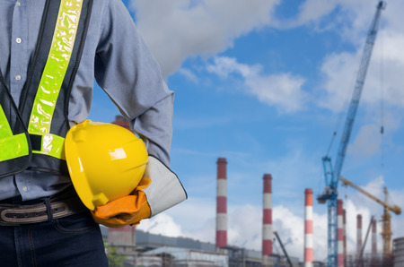 Engineer holding a yellow helmet with a coal power plant in the background.の写真素材
