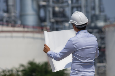 Engineer wearing white helmet standing on refinery background.
