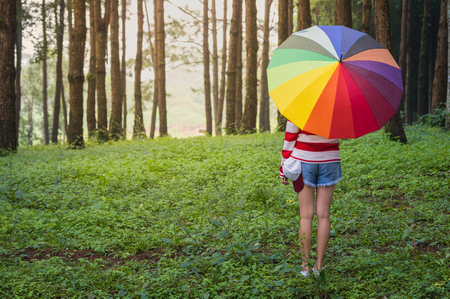 Woman holding colorful umbrellas under the rain fall in the park.の写真素材