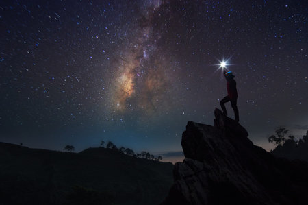 Silhouette of climber or backpacker. In his hand, he held the light up high above his head. Standing...