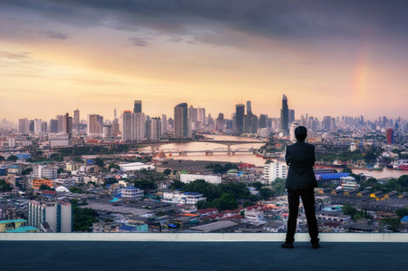 Vision concept. Successful businessman standing with hands crossed on chest, On top of building and looking through Cityscape Skyline Night Light.の写真素材
