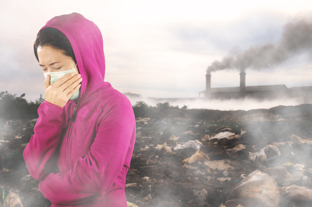 Woman with flu sneezing, woman dressed pink in winter clothing wearing mask to her nose in a cold and flu health concept against air pollution background.の写真素材