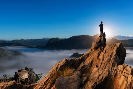 Concept vision, Young businessman wearing comfortable casual suit jacket standing chest hug on top of peak mountain and looking forwards, success, competition and leader concept.の写真素材