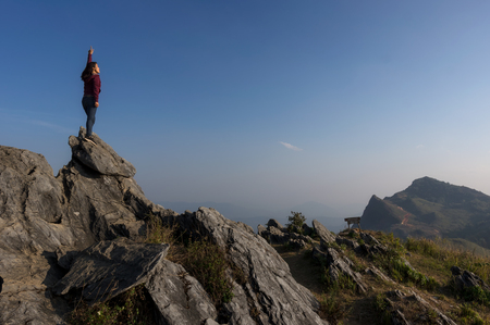 Women tourists standing at the top of the rock, Beautiful view point Sunset of travel place at Doi Pha Tang, Chiang Rai's Hidden Paradise,Thailand.の写真素材