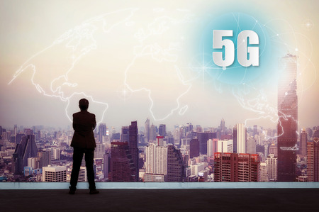 5G network wireless systems and internet of things with successful with businessman standing on top of building and looking through Cityscape Skyline, Connect global wireless devices.の写真素材