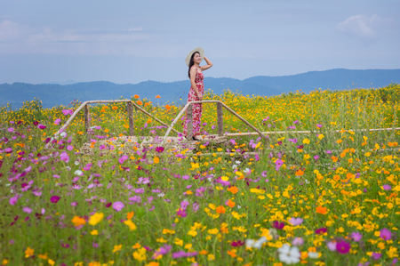 Beautiful woman in nature flower, Her wear white dresses and red hat in Tung Bua Tong Mexican sunflower field in Mae Moh Coal Mine, Lampang Province, Thailand.の写真素材