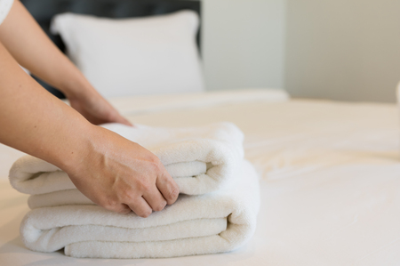 Young hotel maid putting soft towels, bedding and towels in a hotel cleaner was placed on a clean white blanket on the bed with a pillow in the bedroom the morning.の写真素材