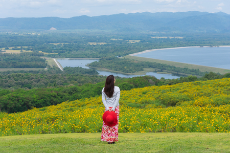 Beautiful woman in nature flower, Her wear white dresses and red hat in Tung Bua Tong Mexican sunflower field in Mae Moh Coal Mine, Lampang Province, Thailand.の写真素材