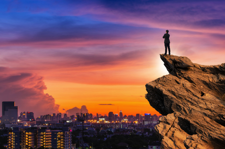 Concept vision, Businessman wearing comfortable casual suit jacket standing chest hug on top of peak mountain and looking forwards with cityscape background, success, competition and leader concept.の写真素材