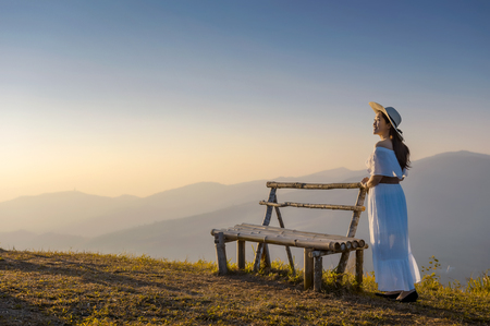 Asian women in white dresses with wide-brimmed hats standing beside the chairs at the morning viewpoint, Ban Rong Kla, Phitsanulok (Phu Lom Lo)の写真素材