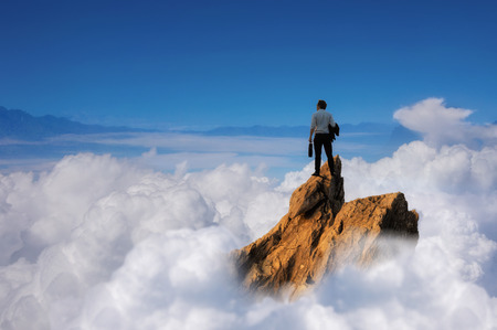 Success concept, Businessman standing on top of peak mountain cliff over the clouds  and looking forwards, competition and leader concept.の写真素材