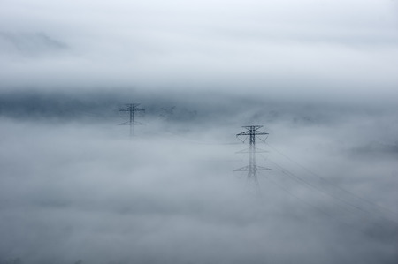 High voltage power transmission towers in fog on mountain mae moh lampang.の写真素材