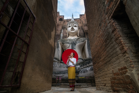 Beautiful woman with Thai traditional dress and Ancient architecture of Buddhist temples in Sukhothai Historical Park. Statue of Buddha at Wat Si Chum (temple) Thailandの写真素材