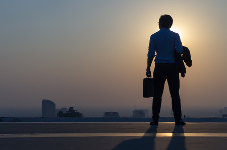 Young businessman wearing a suit stands at the top of the building and looks at modern high-rise buildings, business vision concepts.の写真素材