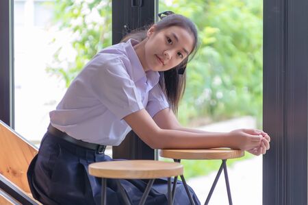 Young Asian college students in uniform beautiful girl relax and smile at coffee shop for learning online, Casual business, social meeting, or education concept.の写真素材