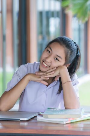Young Asian college students in uniform beautiful girl relax and smile using laptop computer at coffee shop for learning online, Casual business, social meeting, or education concept.の写真素材