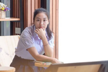 Young Asian college students in uniform beautiful girl relax and smile Read books with relaxed emotions at coffee shop for learning online, Casual business, social meeting, or education concept.の写真素材
