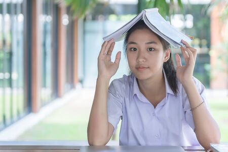 Young Asian college students in uniform beautiful girl relax and smile Read books with relaxed emotions at coffee shop for learning online, Casual business, social meeting, or education concept.の写真素材
