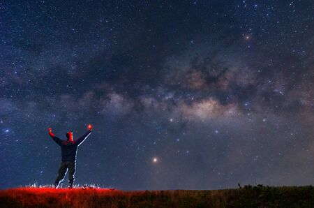 Climber or backpacker with fire in the hand on rocky mountain peak, find the target, search under the stars and Milky Way Galaxy at night, success or winner, leader concept. High iso with Noise.の写真素材