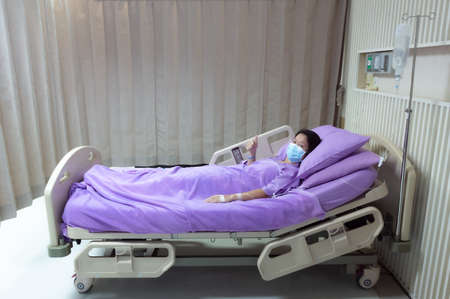 Young Asian female patient is smiling and showing Thumbs up gesture. Patient feels happy and comfortable with treatment and therapy on hospital bed in hospital room. Medical healthcare concept.の写真素材