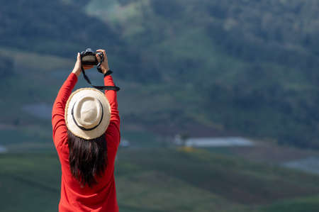 Asian female tourist wearing a bright red shirt taking pictures of beautiful natural scenery.の写真素材