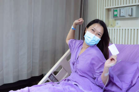 Young Asian female patient is smiling and showing blank credit card, Patient feels happy and comfortable with treatment and therapy on hospital bed in hospital room. Healthcare and Insurance concept.の写真素材