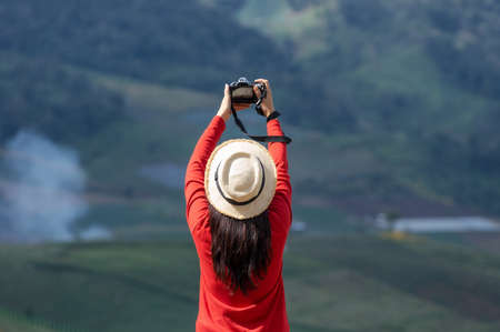Asian female tourist wearing a bright red shirt taking pictures of beautiful natural scenery.の写真素材
