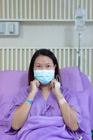 Young Asian female patient is smiling and showing medical mask. Patient feels happy and comfortable with treatment and therapy on hospital bed in hospital room. Medical healthcare concept.の写真素材
