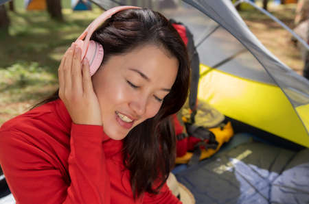 A beautiful woman enjoy listening to music from headphones and use tablet. She sit in a yellow tent. Admiring the nature In the middle of a pine forest beside Lake, Pang Oung ,Mae Hong Son, Thailand.の写真素材