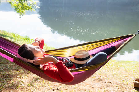 Asian woman happily listening to music in a hammock in a lakeside park, Pang Oung, Mae Hong Son Province, Thailand.の写真素材