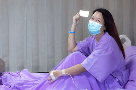 Young Asian female patient is smiling and showing blank credit card, Patient feels happy and comfortable with treatment and therapy on hospital bed in hospital room. Healthcare and Insurance concept.の写真素材