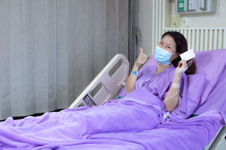 Young Asian female patient is smiling and showing blank credit card, Patient feels happy and comfortable with treatment and therapy on hospital bed in hospital room. Healthcare and Insurance concept.の写真素材