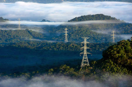Transmission tower in green forest and beautiful morning smooth fog. Energy and environment concept. High voltage power poles.の写真素材