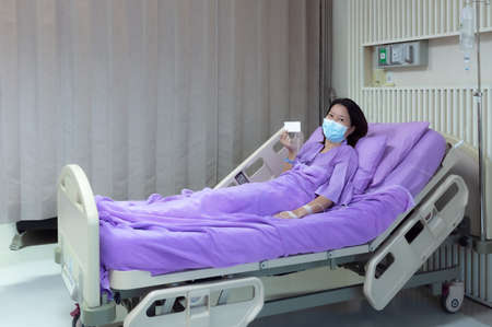 Young Asian female patient is smiling and showing blank credit card, Patient feels happy and comfortable with treatment and therapy on hospital bed in hospital room. Healthcare and Insurance concept.の写真素材
