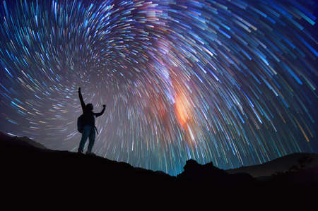 Landscape with Milky Way. Night sky with stars and silhouette of a standing happy man on the mountain, Success or winner, leader concept. High iso with Noise.の写真素材