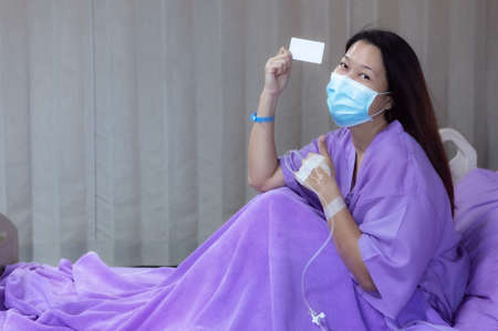 Young Asian female patient is smiling and showing blank credit card, Patient feels happy and comfortable with treatment and therapy on hospital bed in hospital room. Healthcare and Insurance concept.の写真素材
