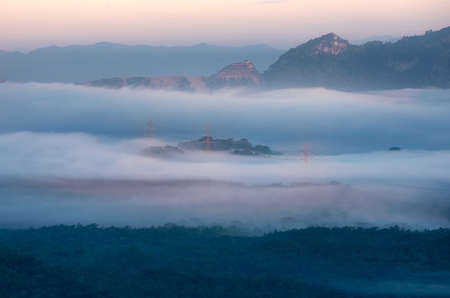 Transmission tower in green forest and beautiful morning smooth fog. Energy and environment concept. High voltage power poles.の写真素材