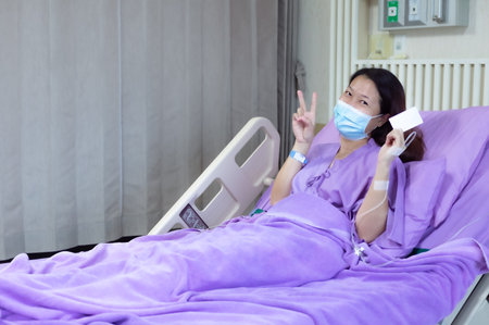 Young Asian female patient is smiling and showing blank credit card, Patient feels happy and comfortable with treatment and therapy on hospital bed in hospital room. Healthcare and Insurance concept.の写真素材