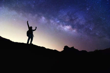 Landscape with Milky Way. Night sky with stars and silhouette of a standing happy man on the mountain, Success or winner, leader concept. High iso with Noise.の写真素材