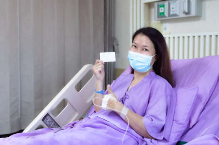 Young Asian female patient is smiling and showing blank credit card, Patient feels happy and comfortable with treatment and therapy on hospital bed in hospital room. Healthcare and Insurance concept.の写真素材