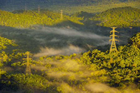 Aerial view Transmission tower in green forest and beautiful morning smooth fog. Energy and environment concept. High voltage power poles. Pang Puay, Mae Moh, Lampang, Thailand.の写真素材