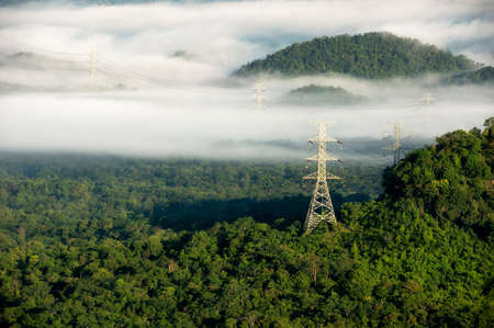 Aerial view Transmission tower in green forest and beautiful morning smooth fog. Energy and environment concept. High voltage power poles. Pang Puay, Mae Moh, Lampang, Thailand.の写真素材