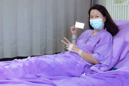 Young Asian female patient is smiling and showing blank credit card, Patient feels happy and comfortable with treatment and therapy on hospital bed in hospital room. Healthcare and Insurance concept.の写真素材