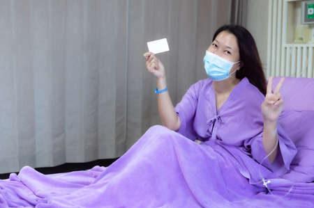 Young Asian female patient is smiling and showing blank credit card, Patient feels happy and comfortable with treatment and therapy on hospital bed in hospital room. Healthcare and Insurance concept.の写真素材