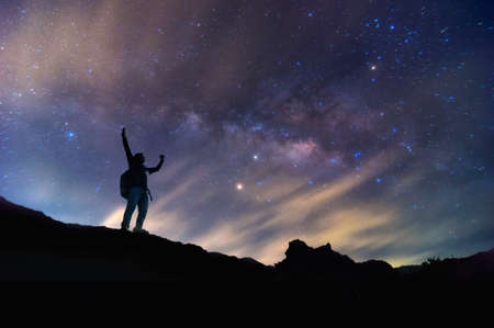 Landscape with Milky Way. Night sky with stars and silhouette of a standing happy man on the mountain, Success or winner, leader concept. High iso with Noise.の写真素材