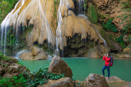 Tourists in red shirts backpacker take a photo and admiring the beauty of Koh Luang Waterfall, Lamphun, Thailand.の写真素材