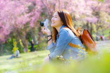Beautiful Young Asian backpacker using vintage camera take a photo and smiling happiness in the midst of spring cherry blossoms bloom Travel lifestyle, world explorer, Asia travel idea.の写真素材