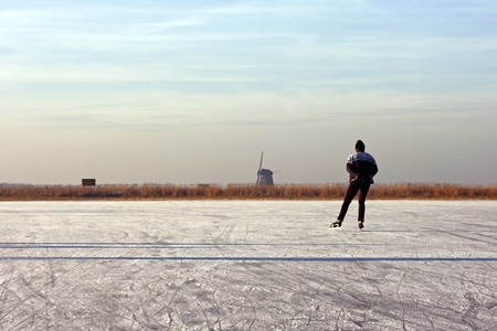 Lonely ice skater on a cold winter in the countryside on frozen ice in the Netherlandsの写真素材