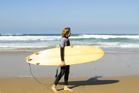 Surfer walking with his surfboard along the beachの写真素材