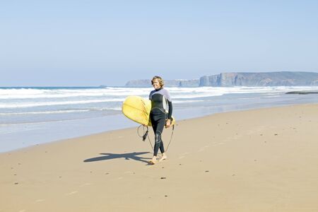 Surfer walking with his surfboard along the beachの写真素材